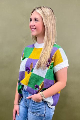 Person wearing a colorful checkered sweater with a green, yellow, and purple pattern against a beige background.