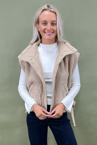 Woman wearing a beige vest over a white sweater on a green background