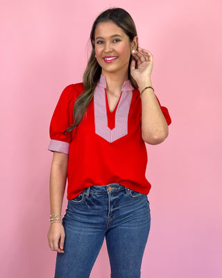 Woman wearing a red blouse with a pink collar against a pink background