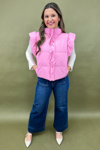 Woman wearing a pink puffer vest over a white shirt with blue jeans on a green background