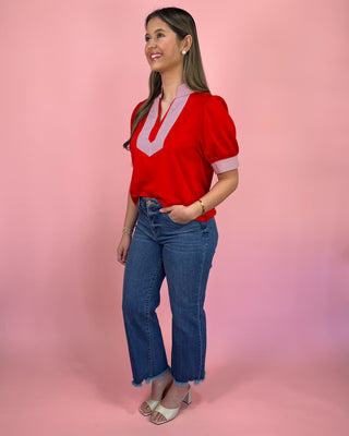 Woman wearing a red blouse with pink accents and blue jeans on a pink background