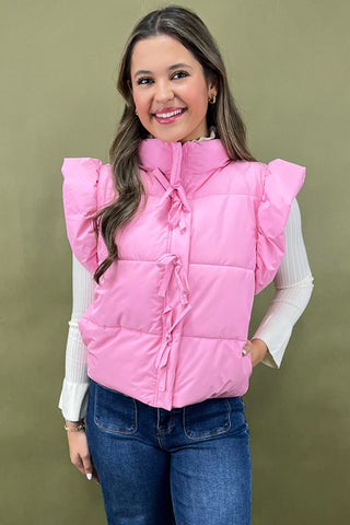 Woman wearing a pink puffer vest with ruffled shoulders against a green background