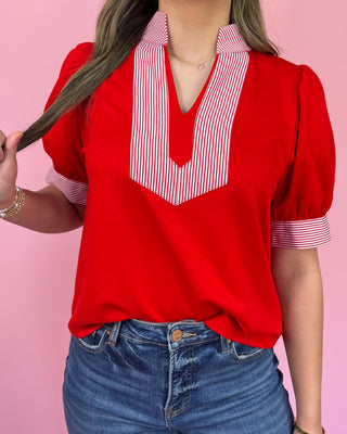 Red blouse with white striped collar worn by a person on a pink background