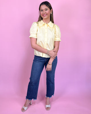 Woman wearing a yellow blouse and blue jeans against a pink background