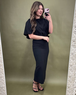 Woman taking a mirror selfie wearing a black outfit against a green background