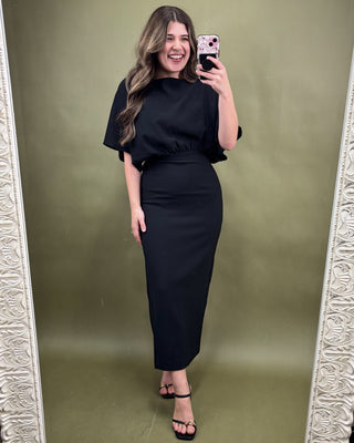 Woman taking a mirror selfie wearing a black outfit against a green background