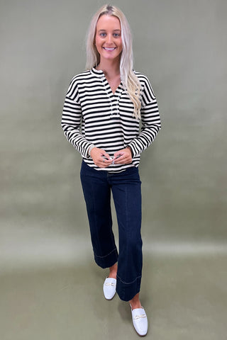 Woman wearing a black and white striped shirt with dark jeans against a plain background