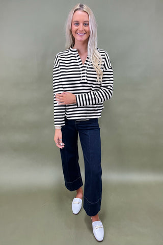 Woman wearing a black and white striped shirt with dark jeans and white shoes on a plain background
