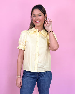Woman wearing a yellow blouse with ruffled collar against a pink background