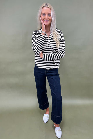 Woman wearing a black and white striped shirt with dark jeans against a plain background