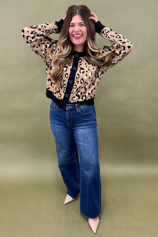 Woman wearing a leopard print blouse and blue jeans against a green background