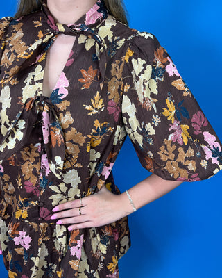 A close-up of a person wearing a brown floral blouse with tie-neck detail and puff sleeves