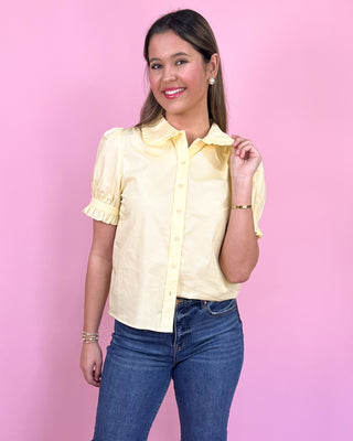 Woman wearing a yellow blouse and blue jeans against a pink background