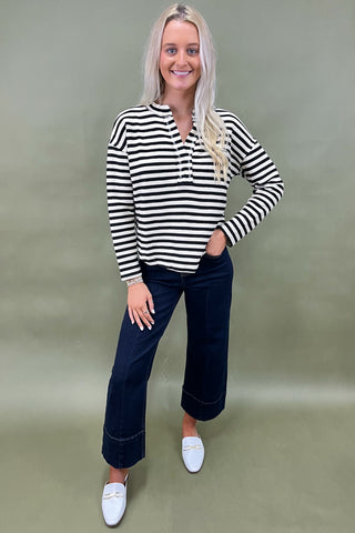 Woman wearing a black and white striped shirt with dark jeans against a plain background