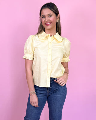 Woman wearing a yellow blouse and blue jeans against a pink background