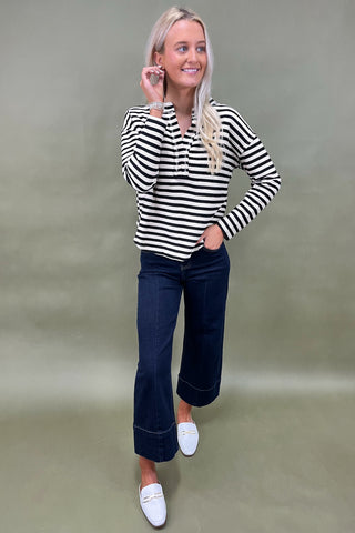Woman wearing a black and white striped shirt and dark blue jeans against a plain background