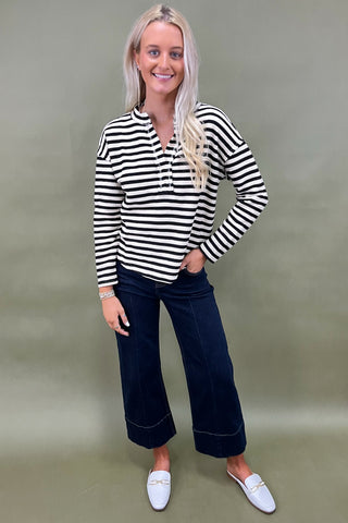 Woman wearing a black and white striped shirt with dark jeans against a plain background