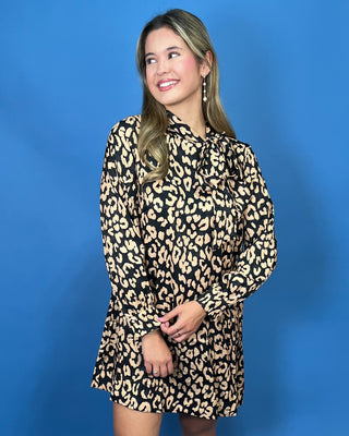 A woman modeling a long-sleeve leopard print dress against a solid blue background.