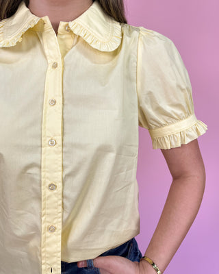 Yellow blouse with ruffled collar and sleeves on a pink background