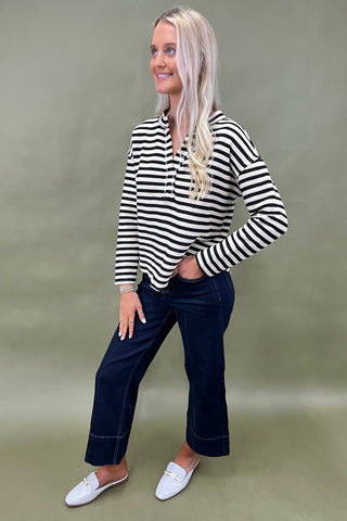Woman wearing a black and white striped shirt and dark jeans against a plain background