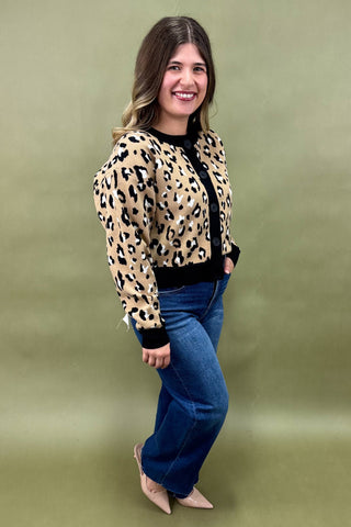 Woman wearing a leopard print jacket and blue jeans against a green background