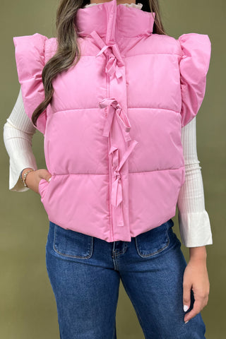Person wearing a pink puffer vest with a white shirt and blue jeans on a green background