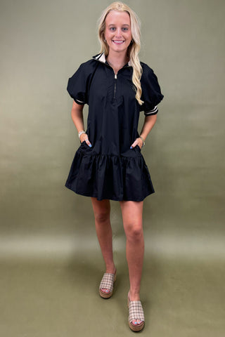 Woman wearing a black dress with white accents against a green background