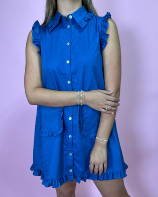Woman wearing a blue dress with ruffled details against a pink background