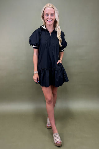 Woman wearing a black dress with white trim against a plain background