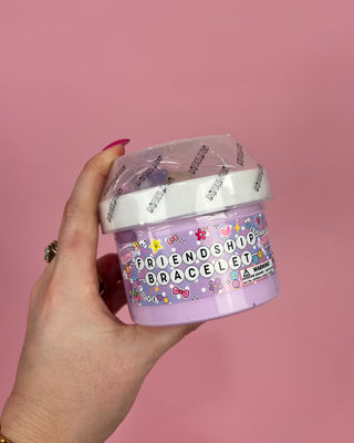 Hand holding a container of friendship bracelets slime against a pink background