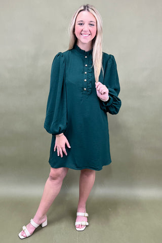 Woman wearing a green dress with long sleeves against a plain background