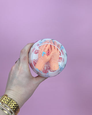 Hand holding a container with a foot-shaped object against a purple background