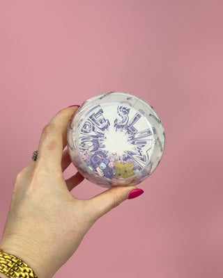 Hand holding a round container with colorful design against a pink background
