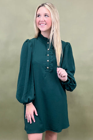 Woman wearing a green dress with long sleeves against a beige background