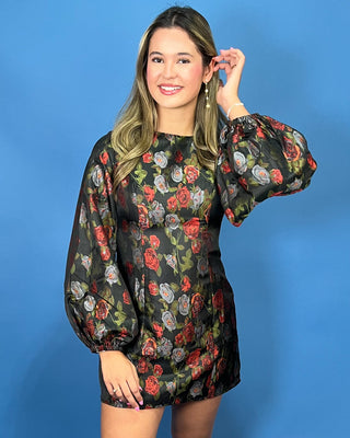 A woman modeling a black long-sleeve mini dress with a vibrant red, pink, and green rose pattern