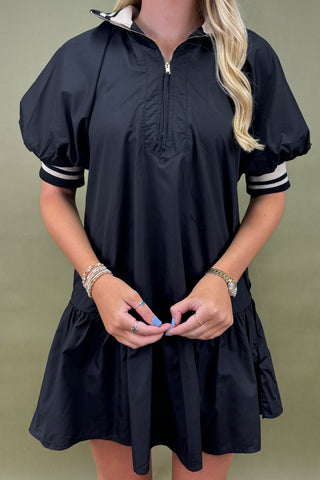 Black dress with white trim worn by a person on a green background
