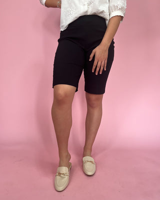 Person wearing black shorts and white shoes on a pink background
