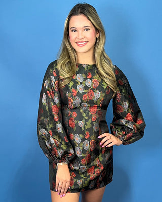 A woman modeling a black long-sleeve mini dress with a vibrant red, green, and gray floral print