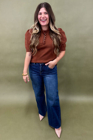 Woman wearing a brown top and blue jeans against a green background
