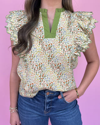 Person wearing a floral blouse with ruffled sleeves against a pink background
