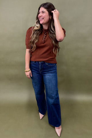 Woman wearing a brown top and blue jeans against a green background
