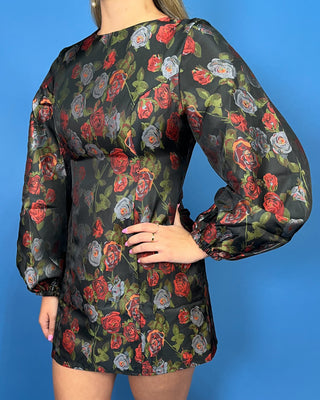 A woman wearing a black long-sleeve mini dress with a red and gray rose pattern