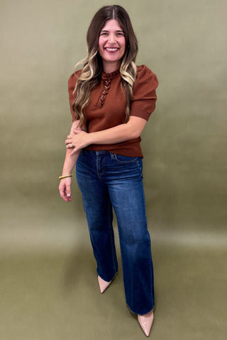 Woman wearing a brown top and blue jeans against a green background