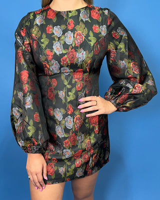 A woman wearing a black long-sleeve mini dress with a red, gray, and green rose pattern