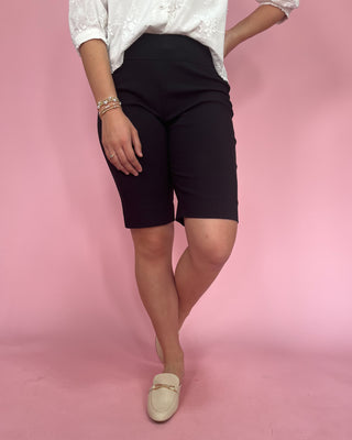 Person wearing black shorts and a white top on a pink background