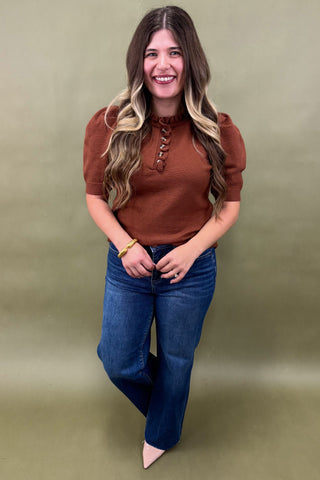 Woman wearing a brown top and blue jeans against a green background