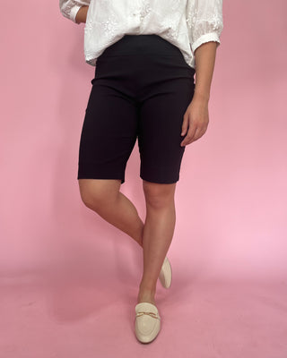Person wearing black shorts and a white top on a pink background