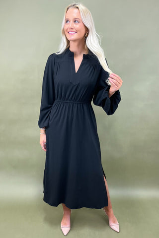 Woman wearing a black dress with a V-neck and long sleeves on a plain background