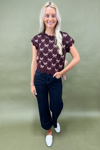 Burgundy knit top with scalloped edges and pink bow pattern styled with dark wide leg cropped jeans and white loafers