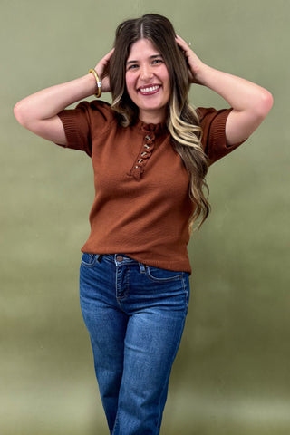Woman wearing a brown top and blue jeans against a green background